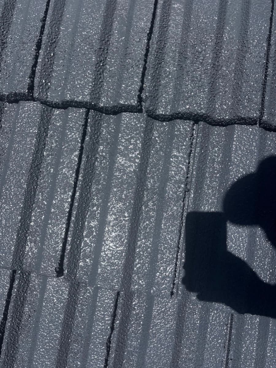 Freshly coated wet tiles close-up with a worker's shadow cast across the surface — still on the job