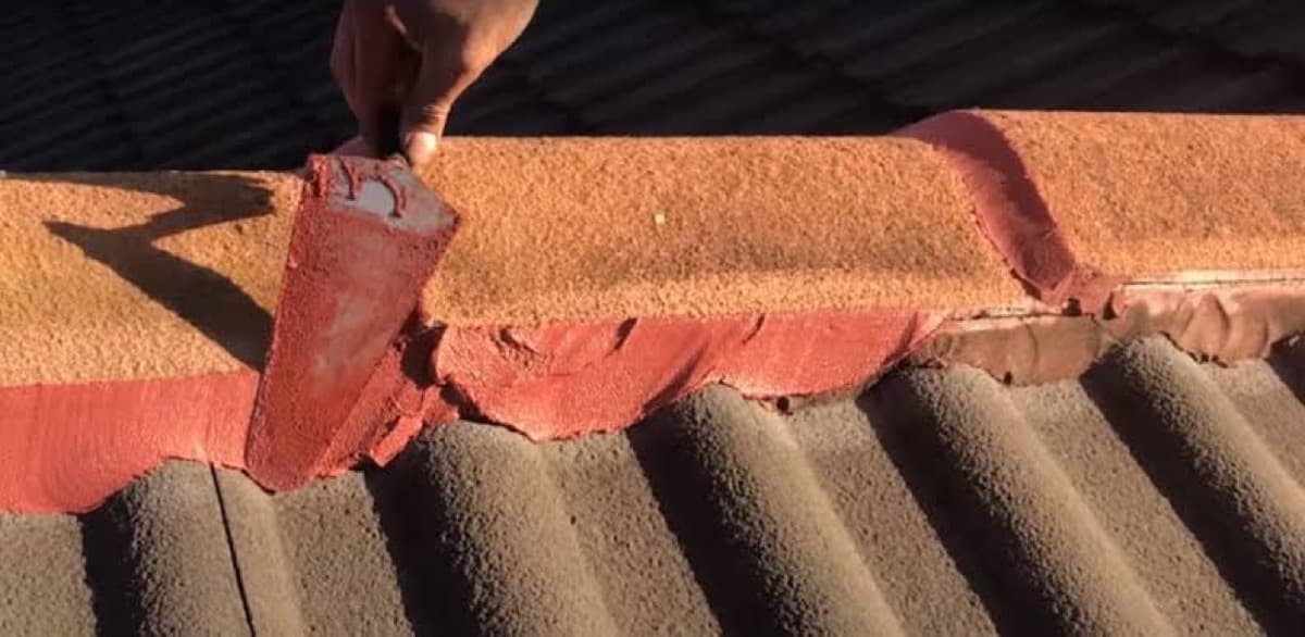 Hand removing a cracked ridge cap tile during a roof repair