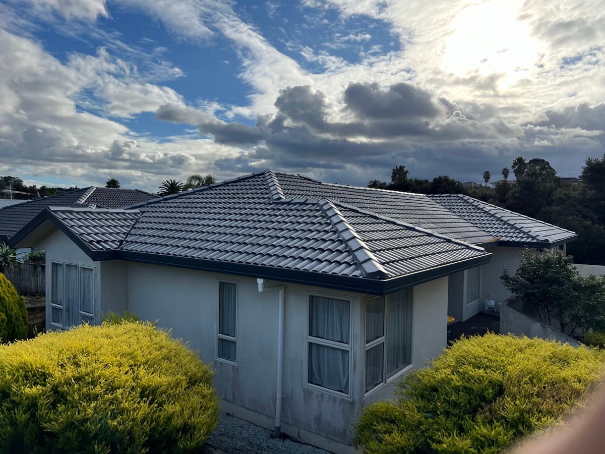 Finished Auckland bungalow with cleanly recoated dark grey hip roof under dramatic sky